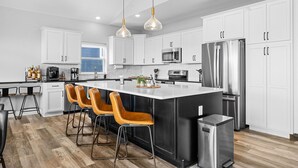 A modern kitchen with white cabinets, stainless steel appliances, and a central island with bar stools. - Lake Views Hot Tub Sauna Arcade Decks Family Stay (Branson)