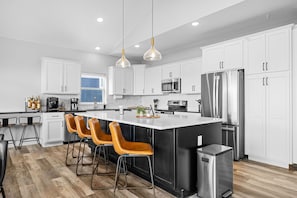 Una cocina moderna con armarios blancos, electrodomésticos de acero inoxidable y una isla central con taburetes de bar.
