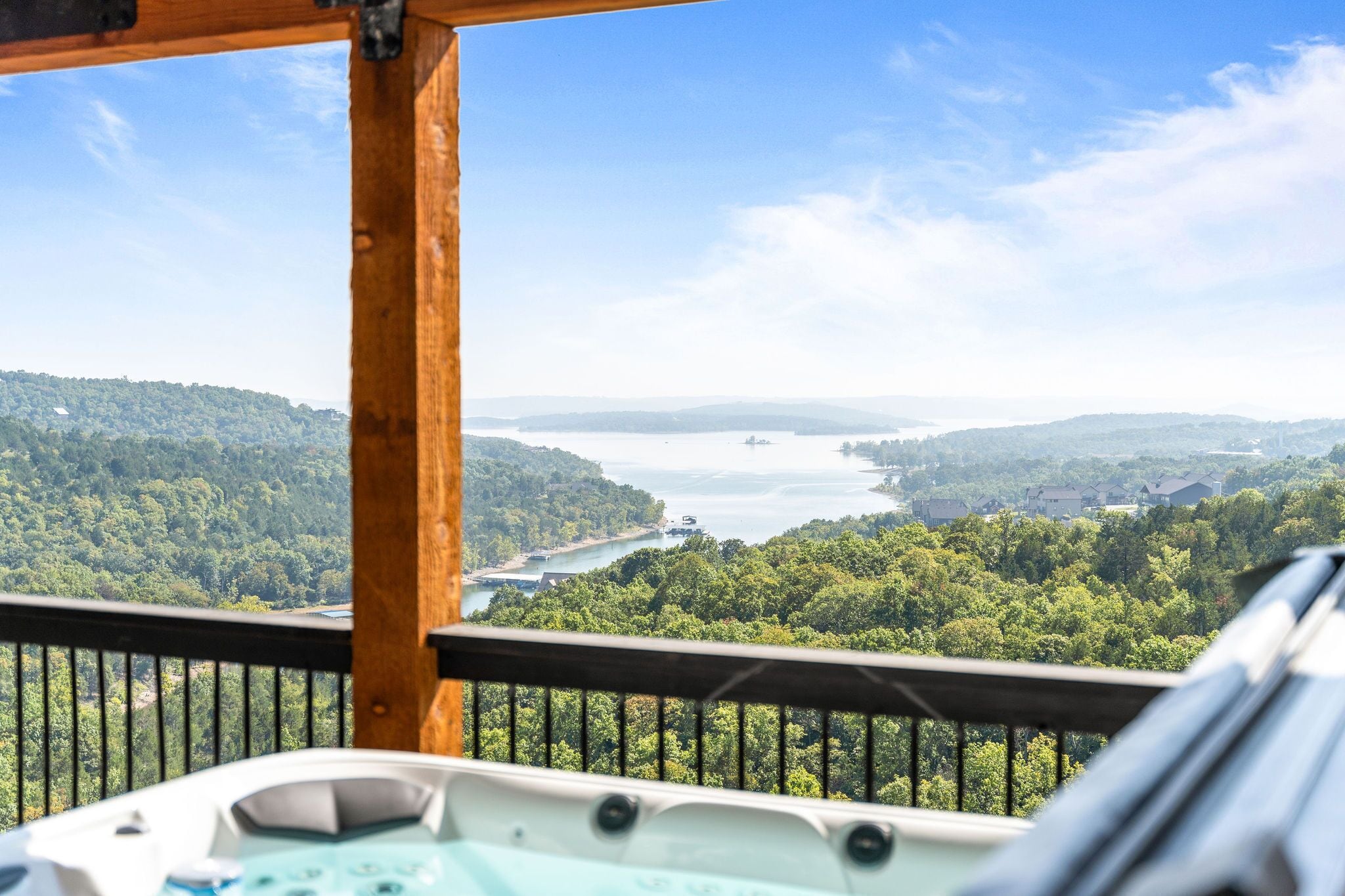 A hot tub on a balcony overlooking a lake surrounded by forest.
