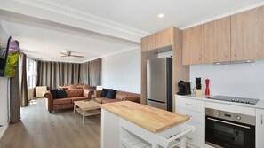 Une chambre d’hôtel moderne avec une table à manger en bois, un canapé en cuir et une kitchenette équipée d’un réfrigérateur et d’une cuisinière.