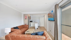 Ett modernt vardagsrum med en soffa i läder, ett litet bord och en tv som är monterad på en skjutbar glasdörr.