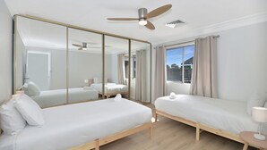 Ett hotellrum med två sängar, en takfläkt, en stor spegel och ett fönster med gardiner.