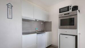 Una cucina compatta con mobili bianchi, lavastoviglie, microonde e forno integrato.