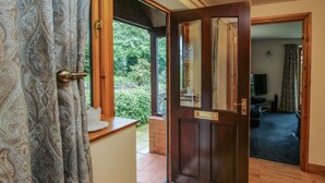Una puerta de madera con un panel de vidrio, un felpudo y vista a una sala de estar con televisor y sofá.
