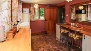 Cocina compacta con armarios de madera, un lavamanos y una ventana. Hay dos taburetes de bar y una pequeña encimera.