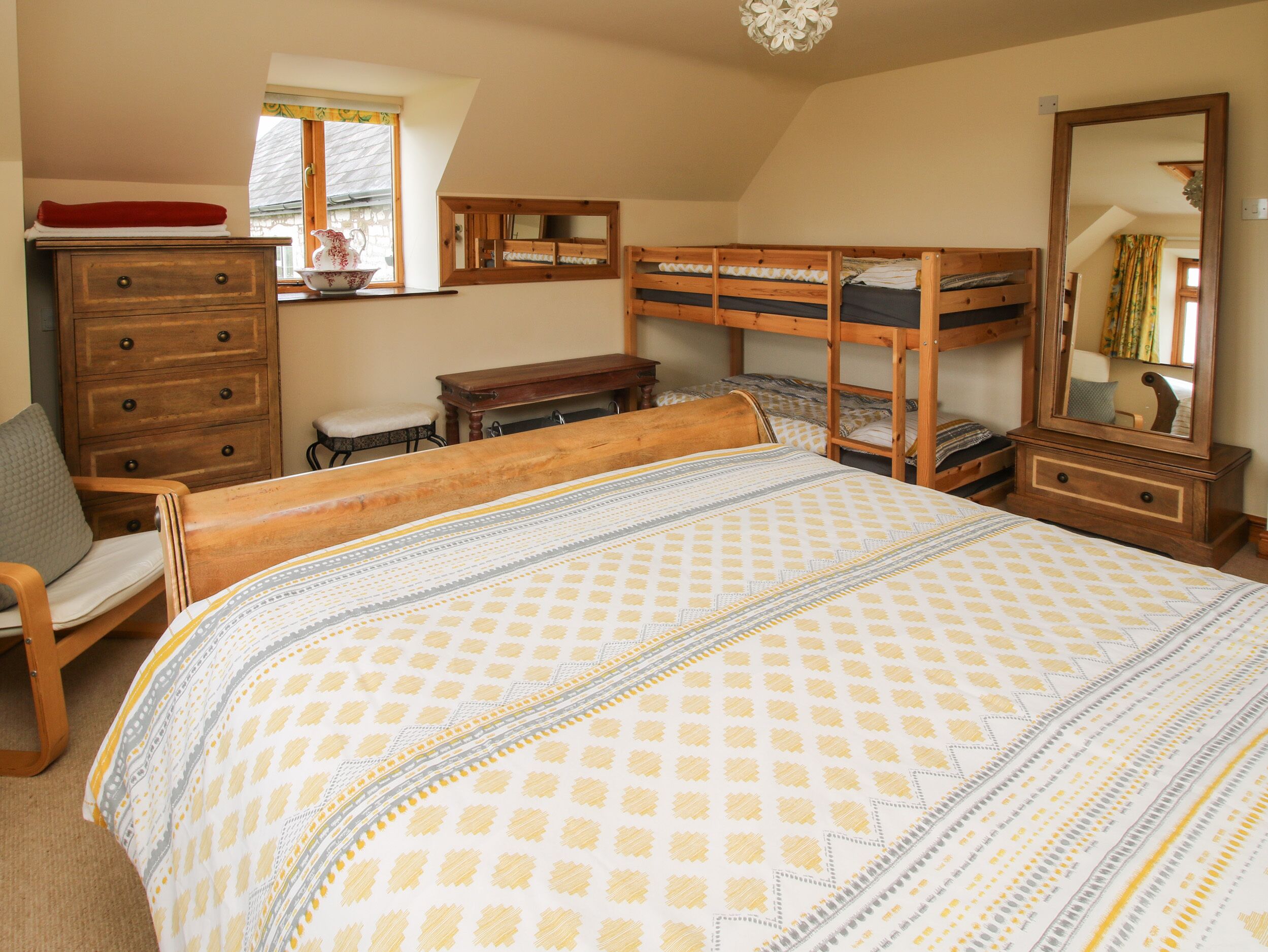Un dormitorio con una cama litera, un aparador de madera, una silla, un escritorio y un espejo grande.