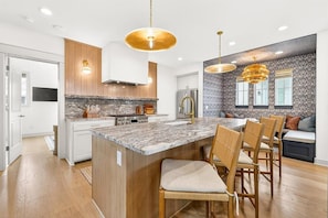 Una cocina moderna con una isla central, armarios de madera, encimeras de granito e iluminación colgante.