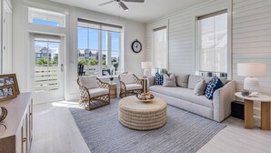 Ein geräumiges Wohnzimmer mit großem Fenster, Deckenventilator und rundem Ottoman.