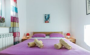 Un dormitorio con cama, dos almohadas, dos lámparas de noche, un cuadro en la pared y una ventana con cortinas.