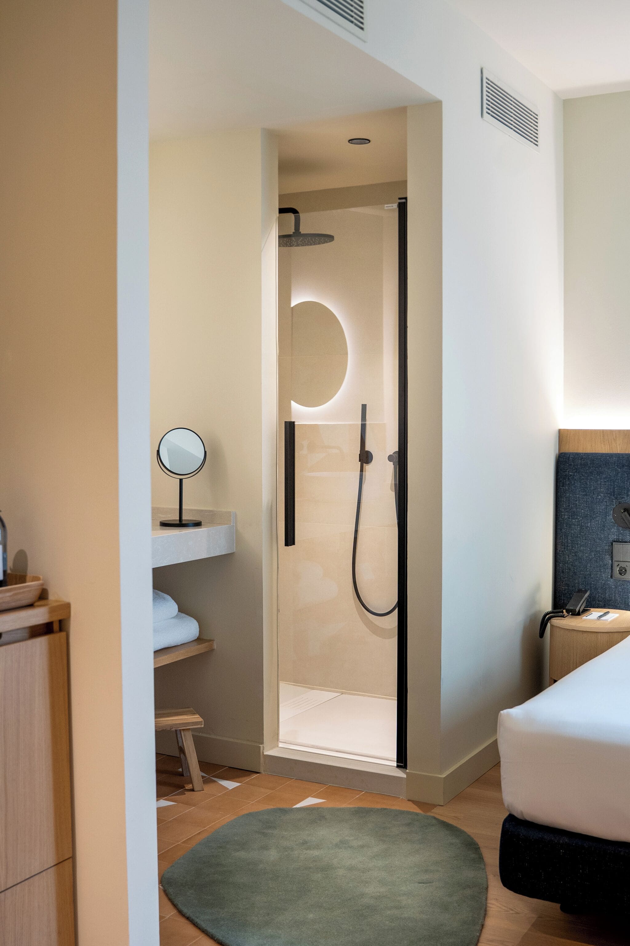 A modern bathroom with a glass-enclosed shower, a round mirror, and a wooden vanity.