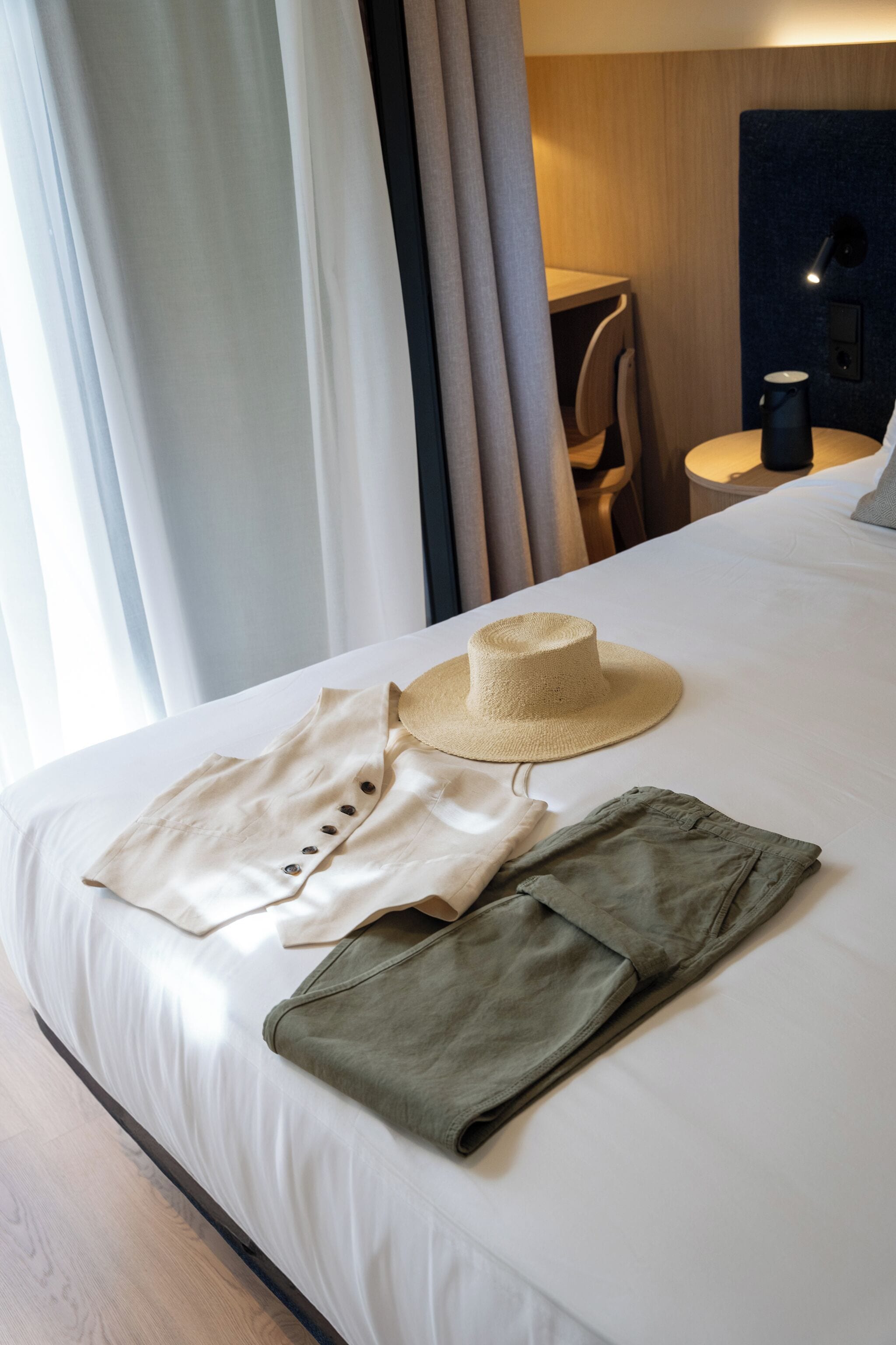Una cama bien hecha con un sombrero de paja, una camisa de color claro y pantalones verdes doblados encima.