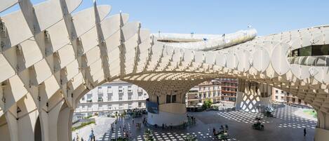 A spacious plaza with a unique architectural canopy structure, surrounded by greenery and a central fountain.