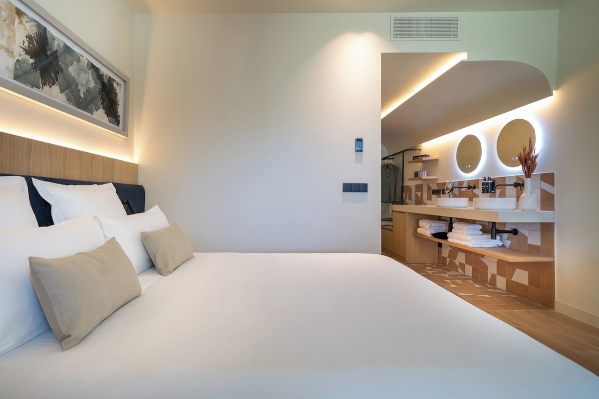 Una habitación de hotel moderna con una cama grande, un baño con tocador y una obra de arte colgada en la pared.
