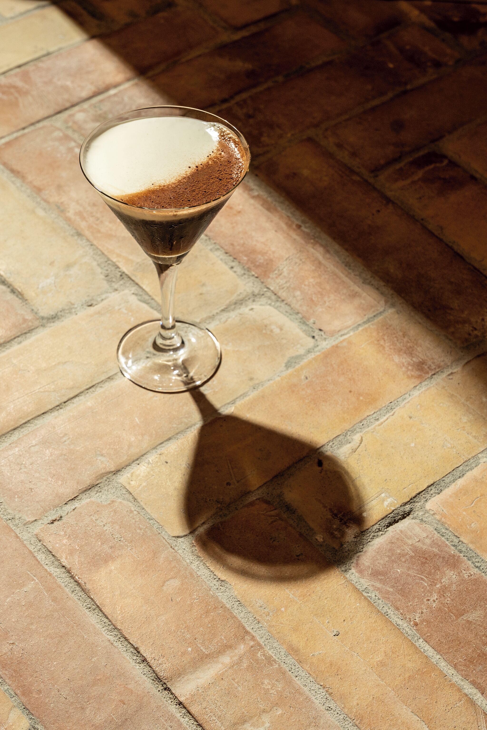 A martini glass with a frothy top on a tiled floor.