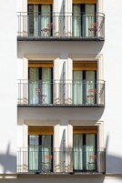 A multi-story building with balconies, each featuring a chair and a window with a curtain.