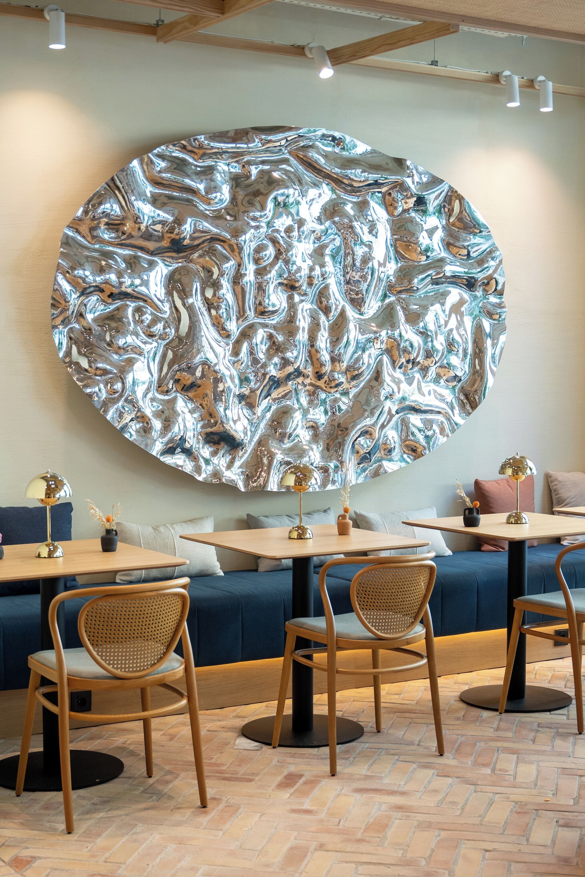 A modern interior with a large metallic wall art, wooden tables, and woven chairs.
