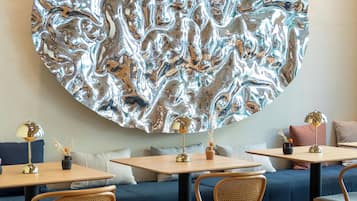 A modern interior with a large metallic wall art, wooden tables, and woven chairs.