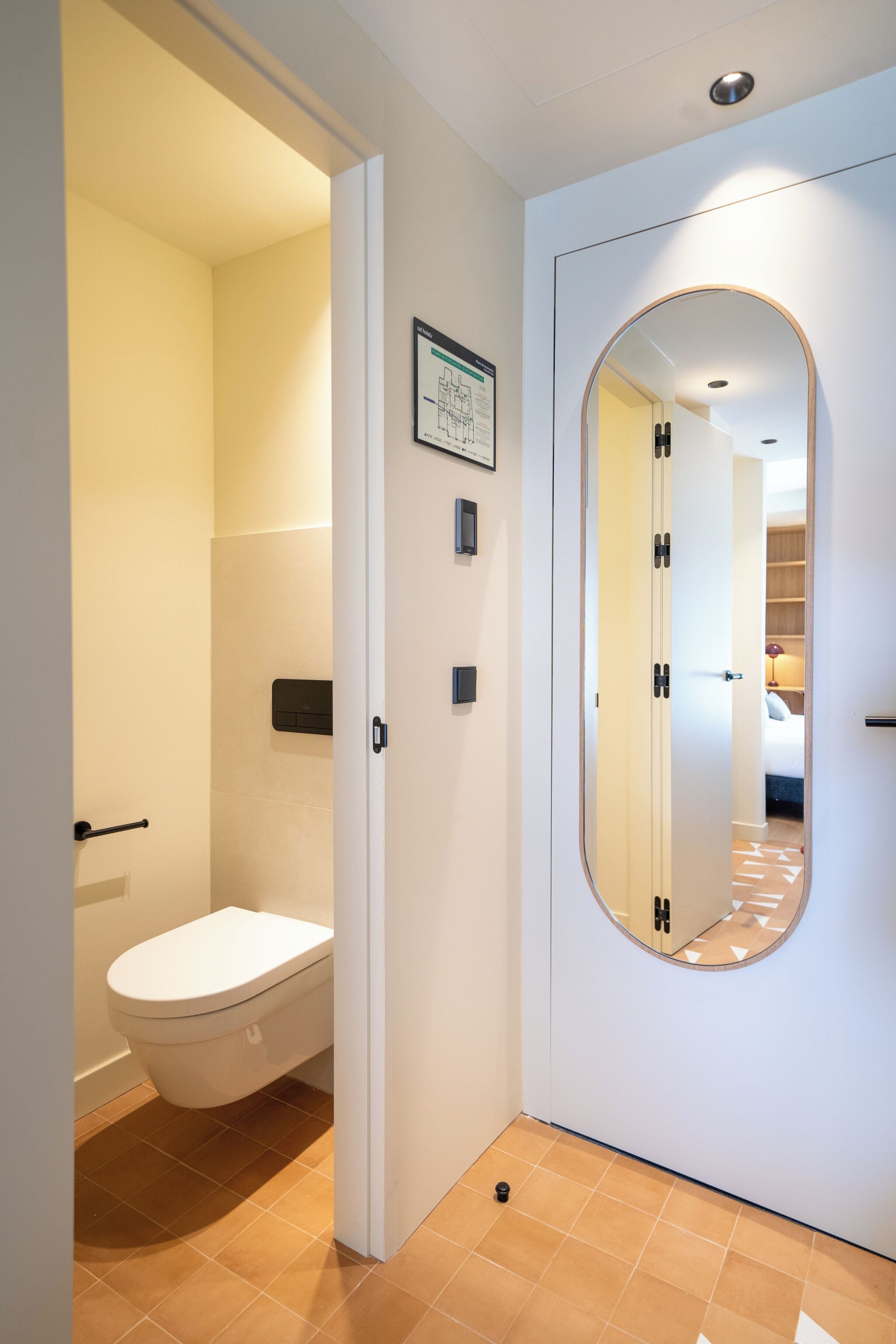 A modern bathroom with a toilet, a mirror, and a door leading to another room.
