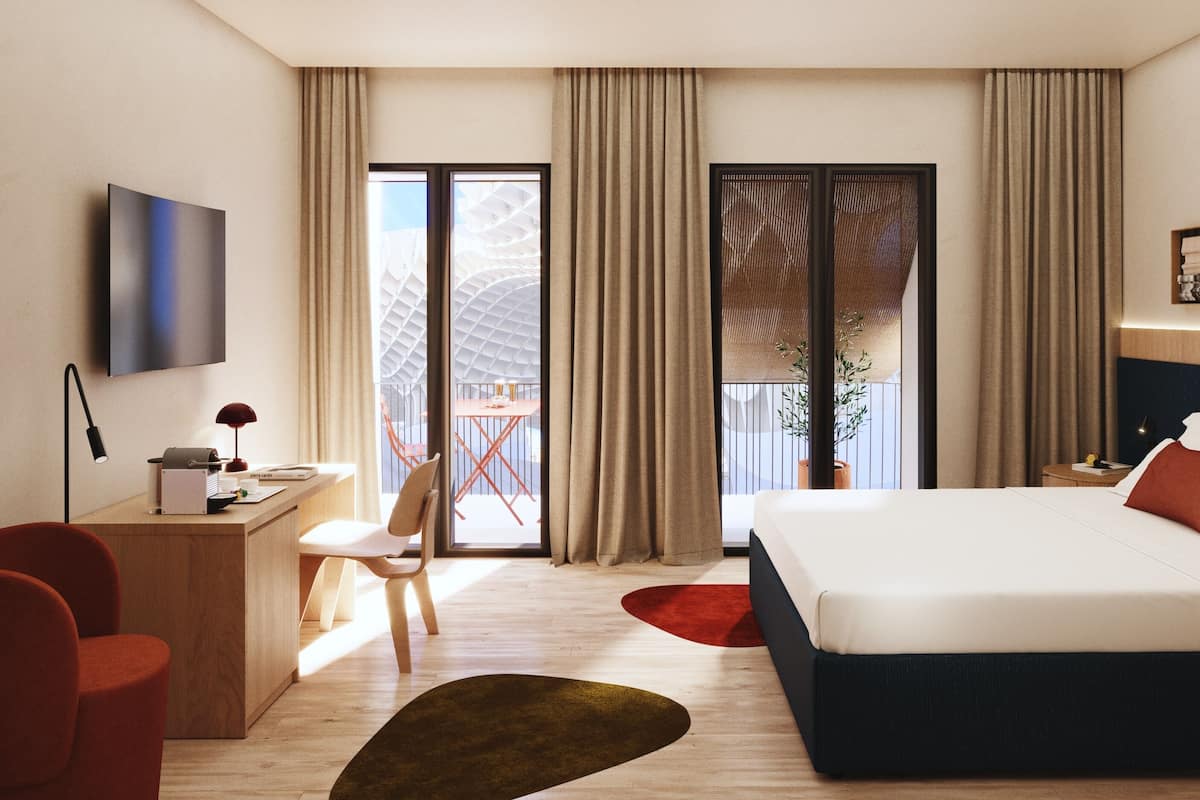 A modern hotel room with a bed, desk, chair, and a view of the outside balcony.