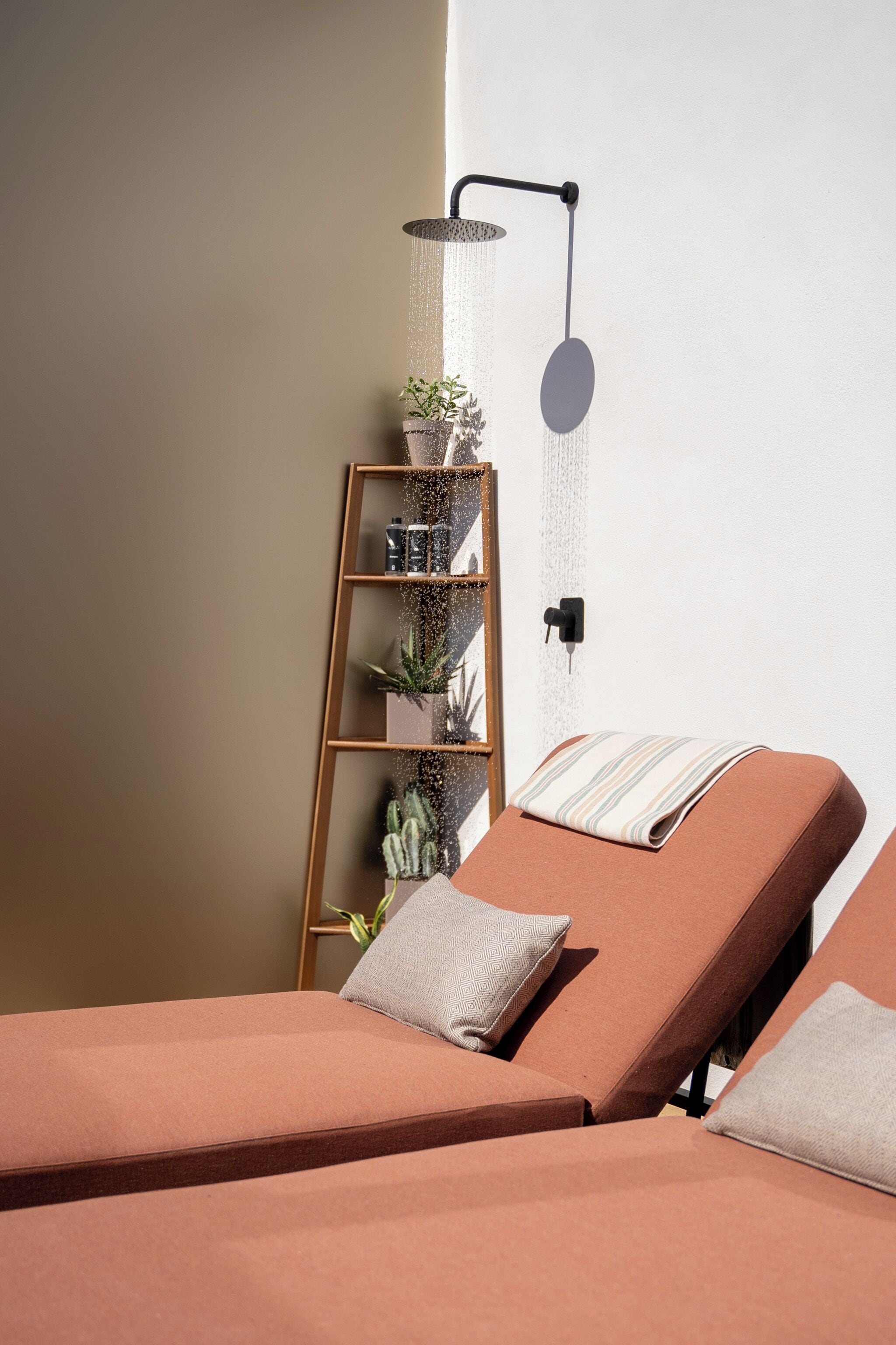 A spa room with two massage chairs, a wall-mounted shower, and a shelf with plants and toiletries.