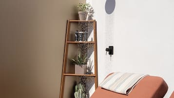 A spa room with two massage chairs, a wall-mounted shower, and a shelf with plants and toiletries.