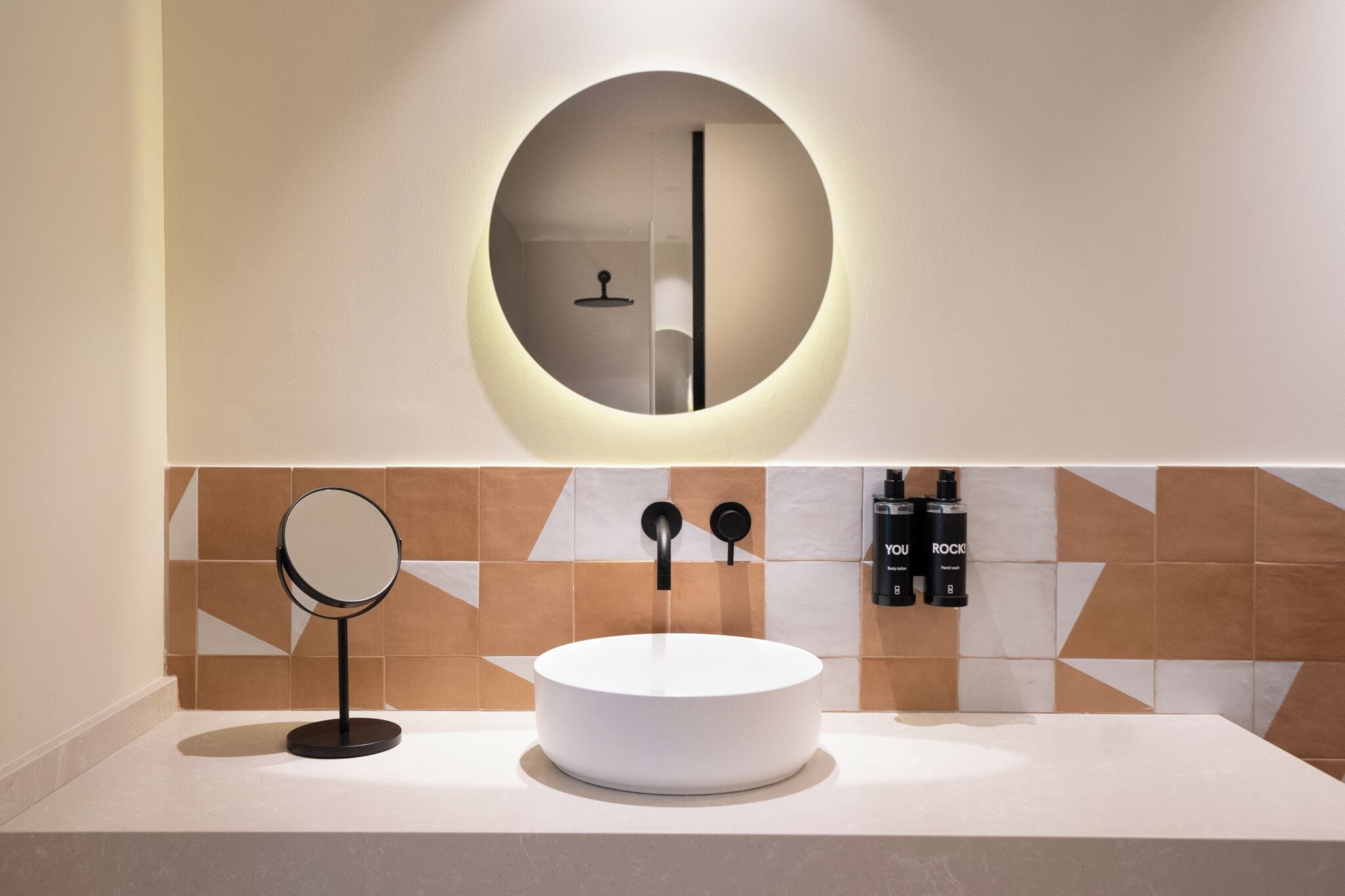 A modern bathroom with a round mirror, a white sink, and a wall-mounted towel rack.