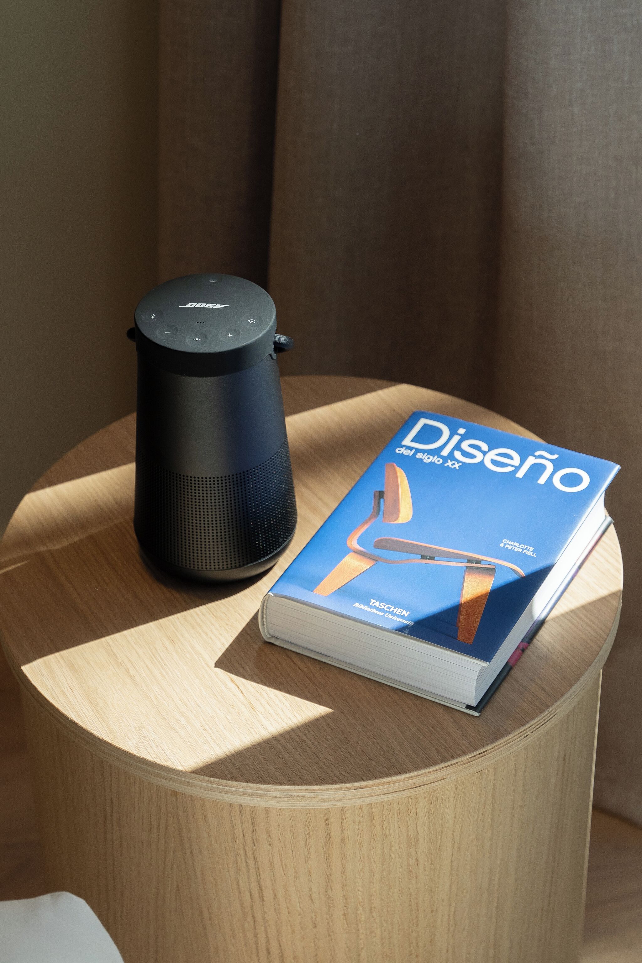 Un altavoz inteligente negro y un libro titulado 'Diseño del siglo xx' sobre una mesa de madera.