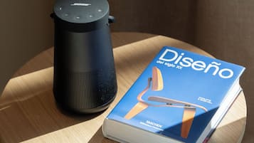 Un altavoz inteligente negro y un libro titulado 'Diseño del siglo xx' sobre una mesa de madera.