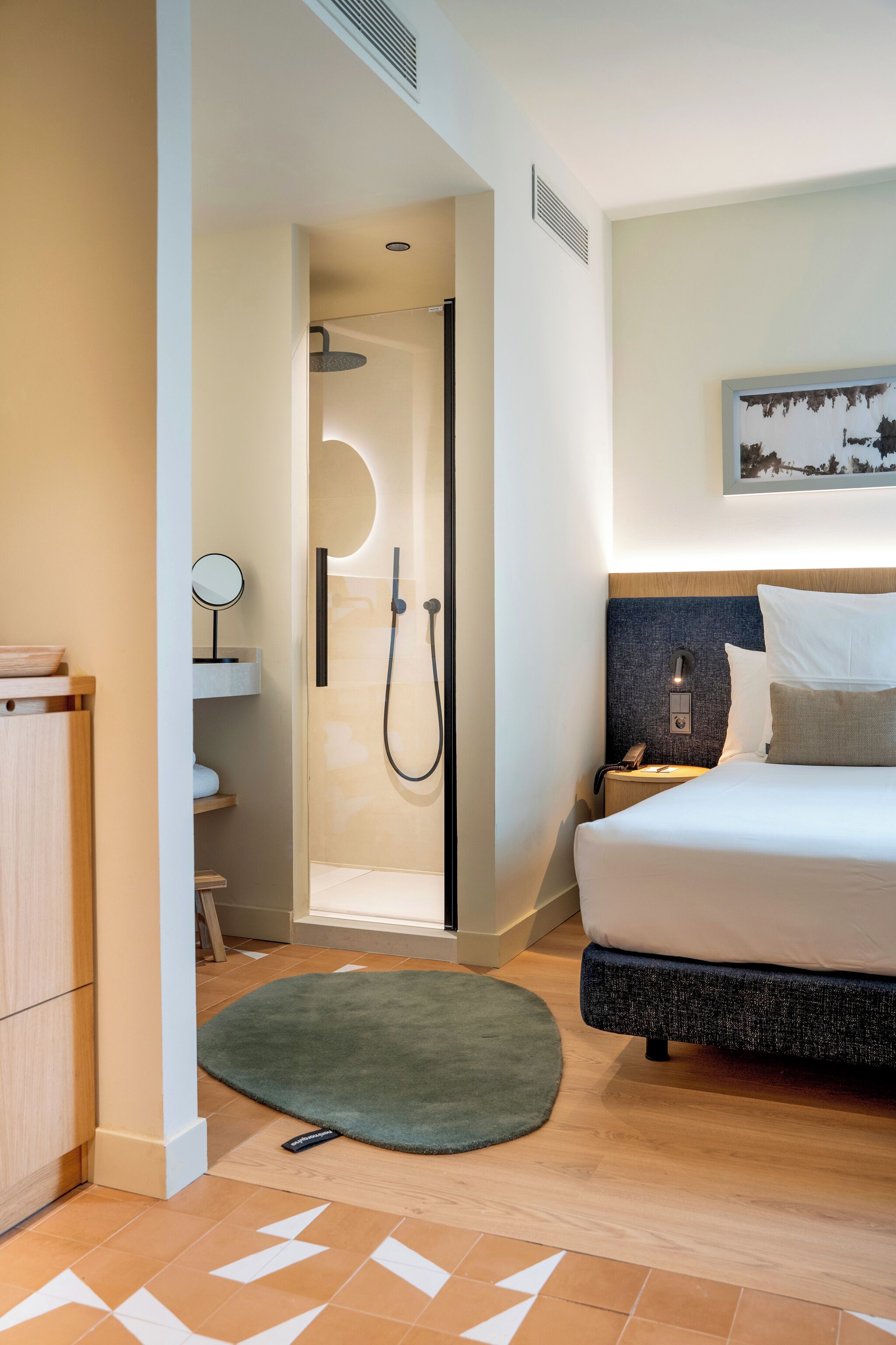 Et moderne hotelværelse med seng, sengebord og bruseområde.