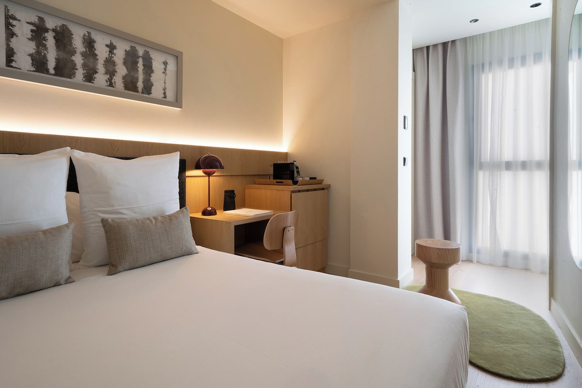 A hotel room with a large bed, a desk, a chair, a lamp, and a framed picture on the wall.