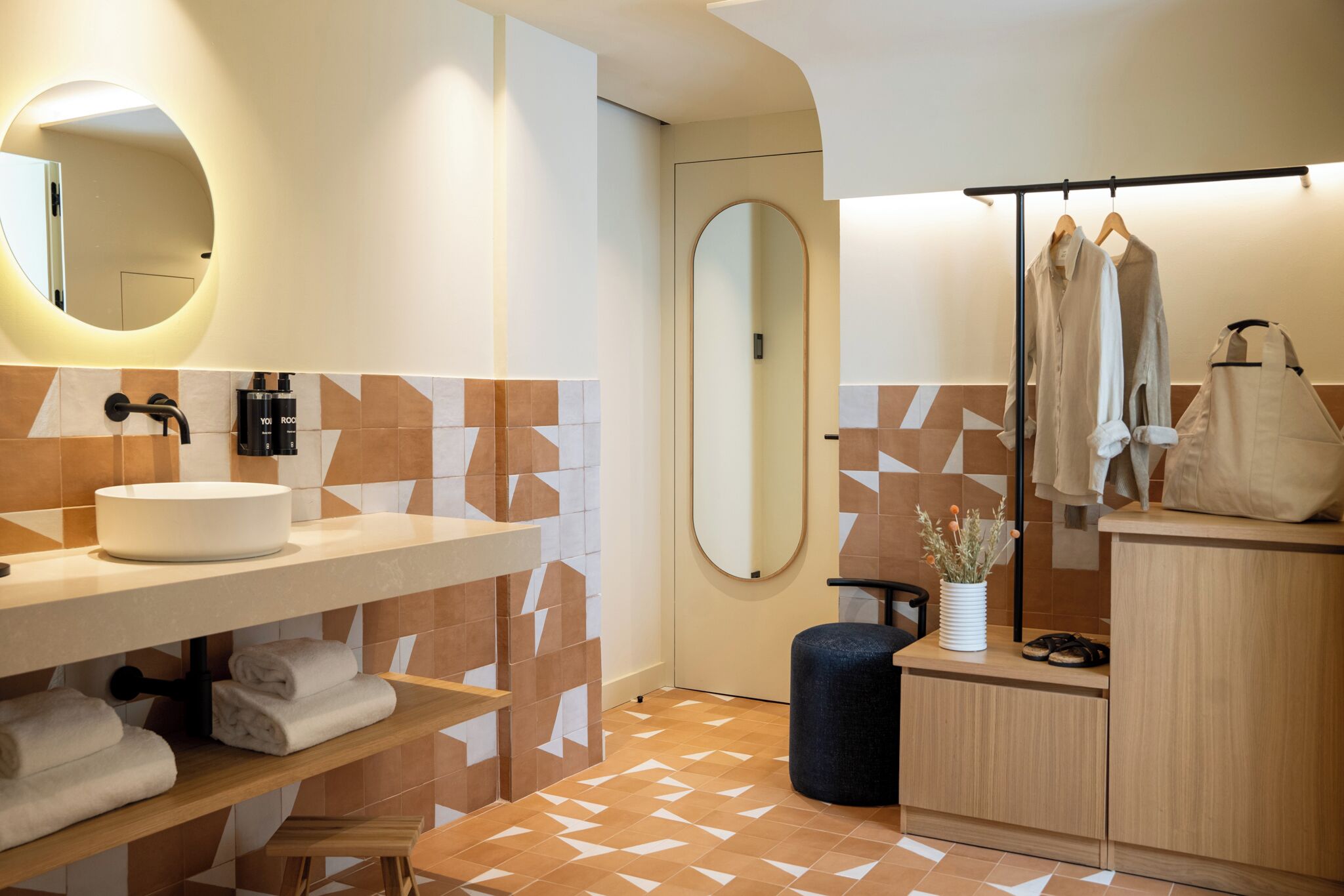 Un baño moderno con un espejo redondo, un lavabo y un perchero para toallas.