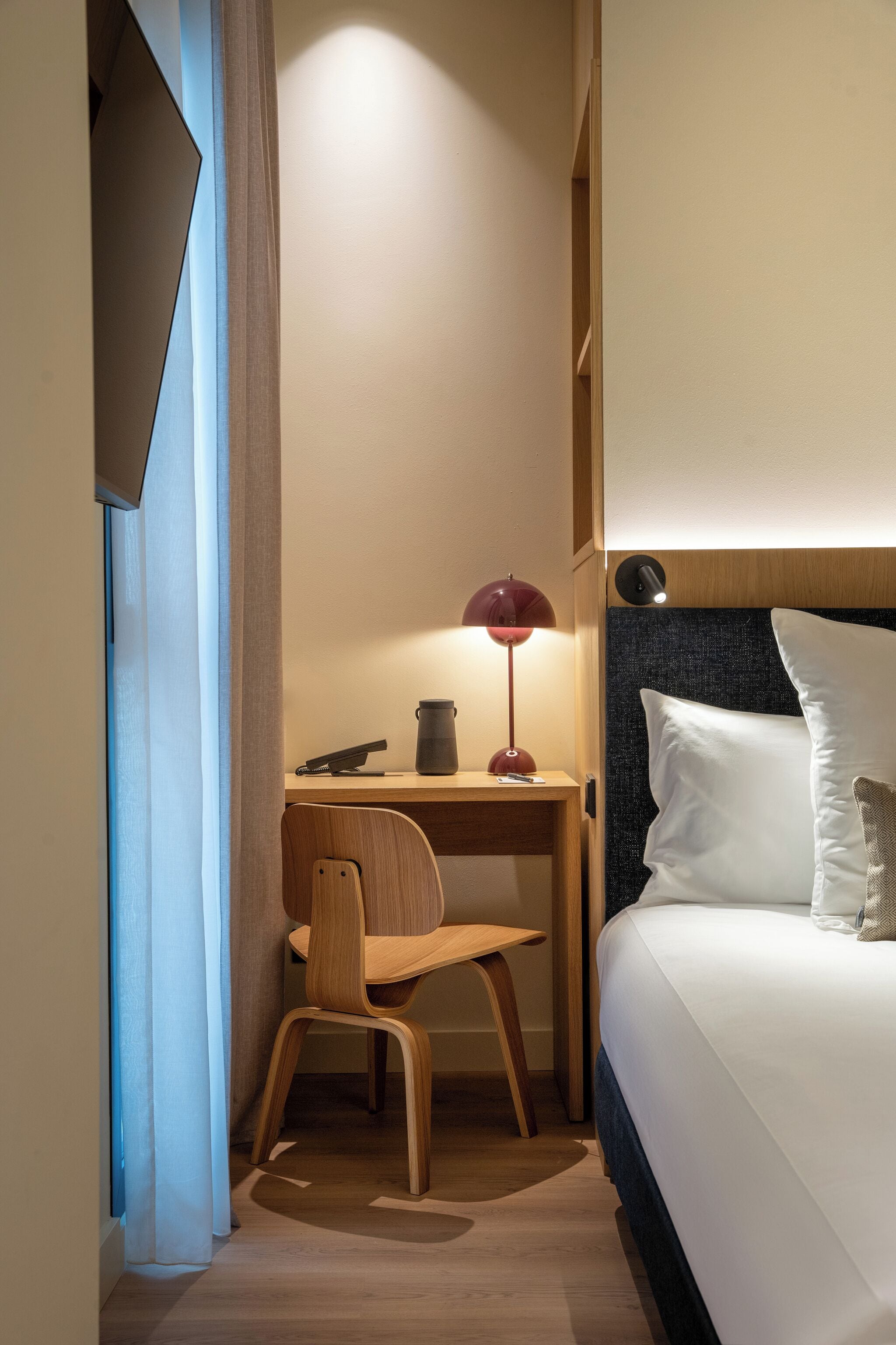 A hotel room with a bed, a desk with a lamp, and a chair.