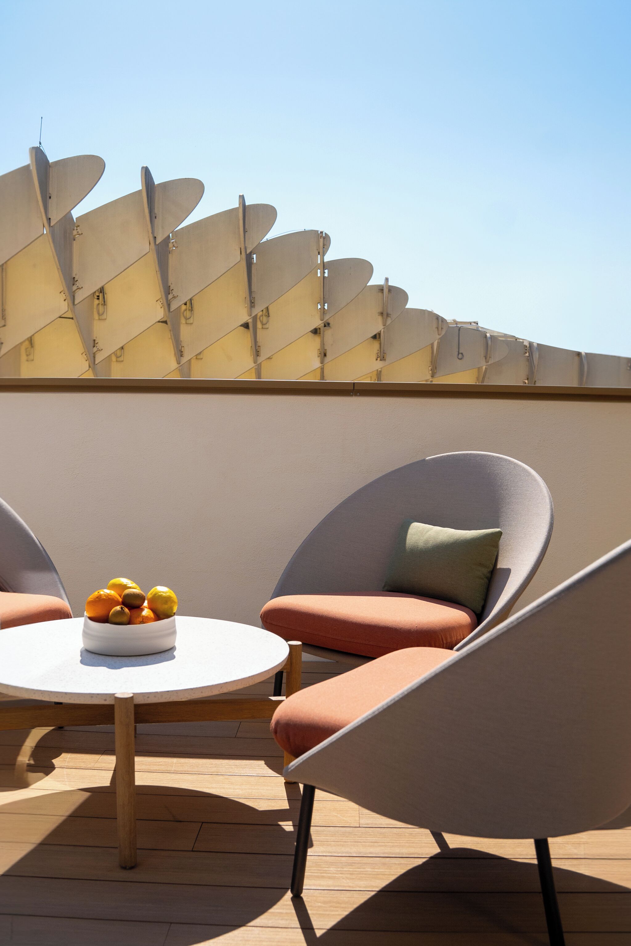 A modern outdoor seating area with two chairs and a round table, featuring a bowl of fruit.