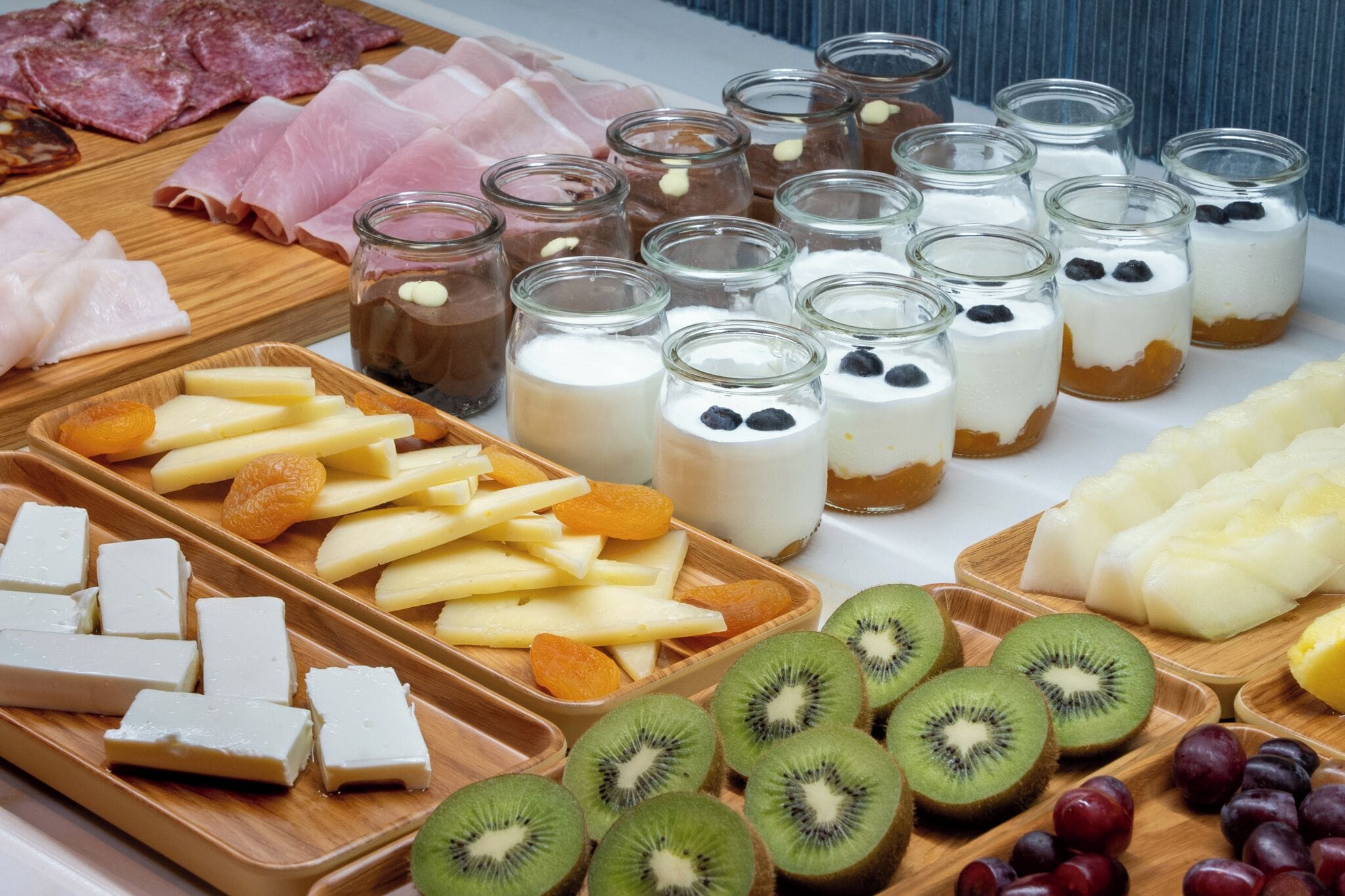 A variety of food items including meats, cheeses, fruits, and desserts on a wooden board.