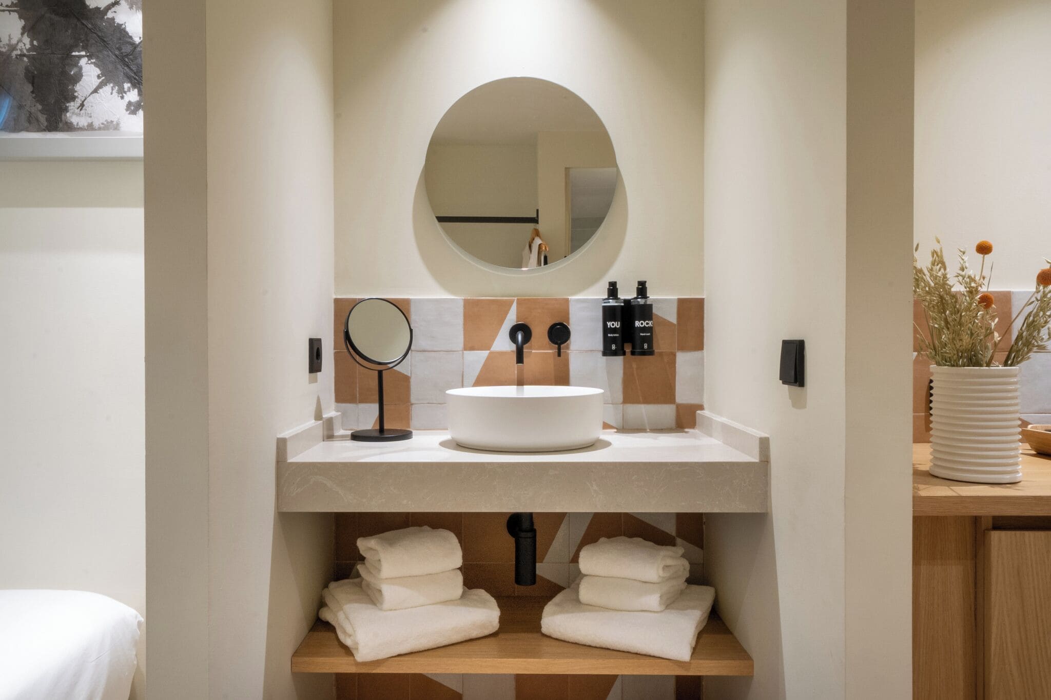 Een moderne badkamer met een ronde spiegel, een rond wastafel en een handdoekhouder.
