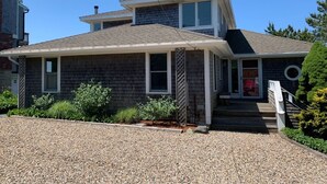 A two-story house with a covered front porch, a small front yard, and a gravel driveway. - Stunning Waterfront in Wellfleet (CS0024) (Wellfleet)