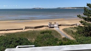A beach with a wooden walkway leading to a sandy area, surrounded by greenery and a clear view of the ocean. - Stunning Waterfront in Wellfleet (CS0024) (Wellfleet)