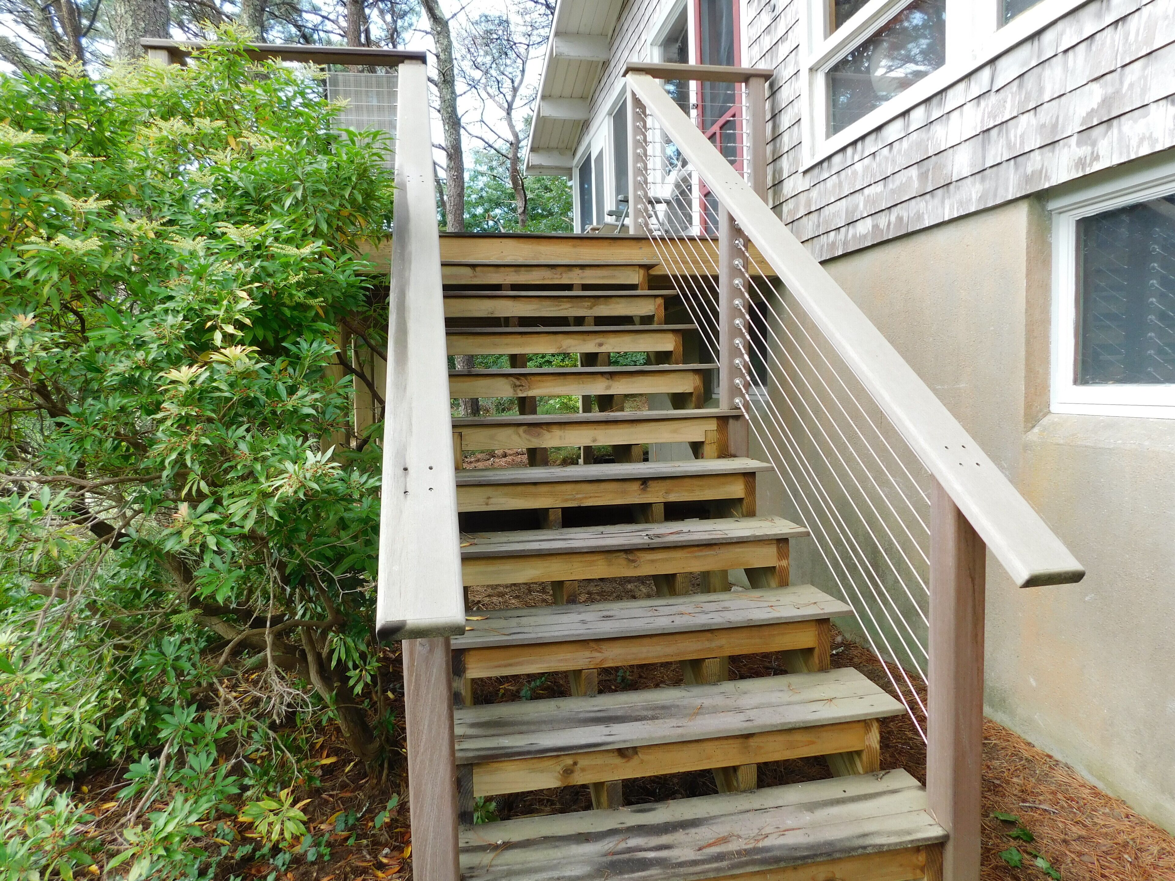 A wooden staircase with a metal handrail leading to a house with a window.