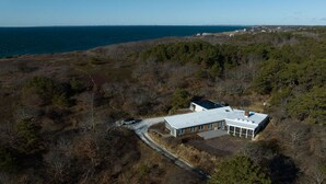 An aerial view of a modern house with a flat roof, surrounded by dense forest and a body of water in the background. - Newly Reno'd GORGEOUS, Water View, Beach Access (CS0034) (Wellfleet)