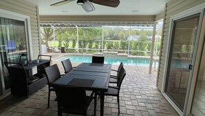 Un patio techado con piscina, mobiliario exterior y ventilador de techo.
