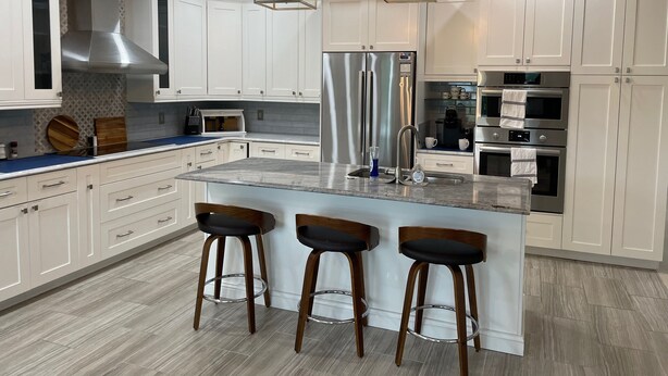 Una cocina moderna con armarios blancos, electrodomésticos de acero inoxidable y una isla central con taburetes de bar.