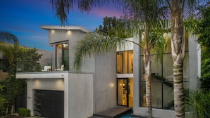 A modern two-story house with a pool, large windows, and a covered outdoor seating area.
