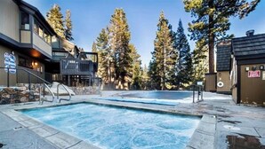 A pool area with a hot tub, surrounded by trees and a building with a stone facade. - Updated tree top cabin retreat! (Mammoth Lakes)