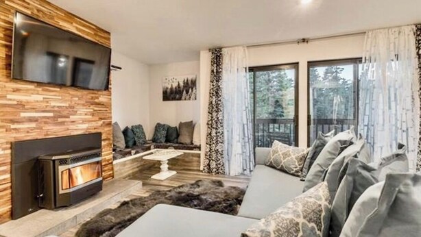 A modern living room with a fireplace, a sofa set, and a large window with curtains. - Updated tree top cabin retreat! (Mammoth Lakes)