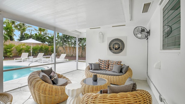 Un espace extérieur aménagé avec des meubles en osier, une piscine et une vue sur les palmiers.