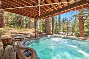 A hot tub under a wooden pergola with a forest view.