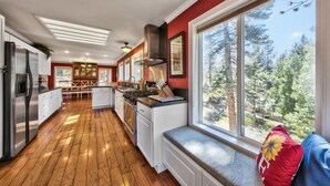 Una cocina moderna con suelo de madera, estufa integrada y un amplio ventanal con vistas a árboles.