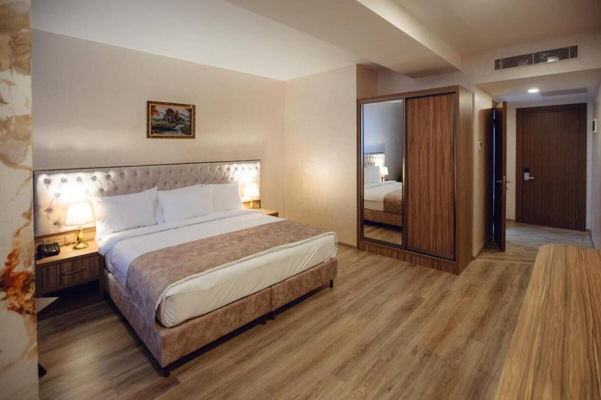 A hotel room with a bed, bedside lamps, a mirror, and a wardrobe.