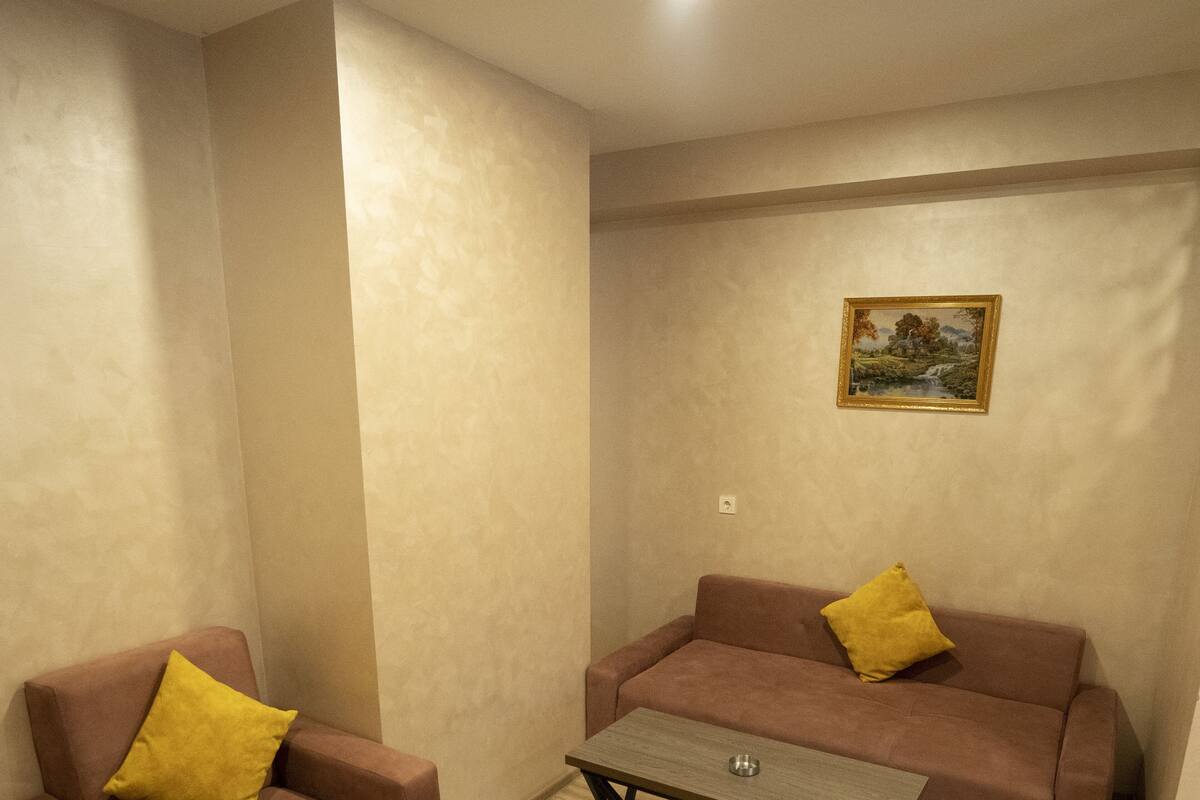 A room with a brown sofa and a matching armchair, both with yellow cushions. There is a wooden coffee table in the center.