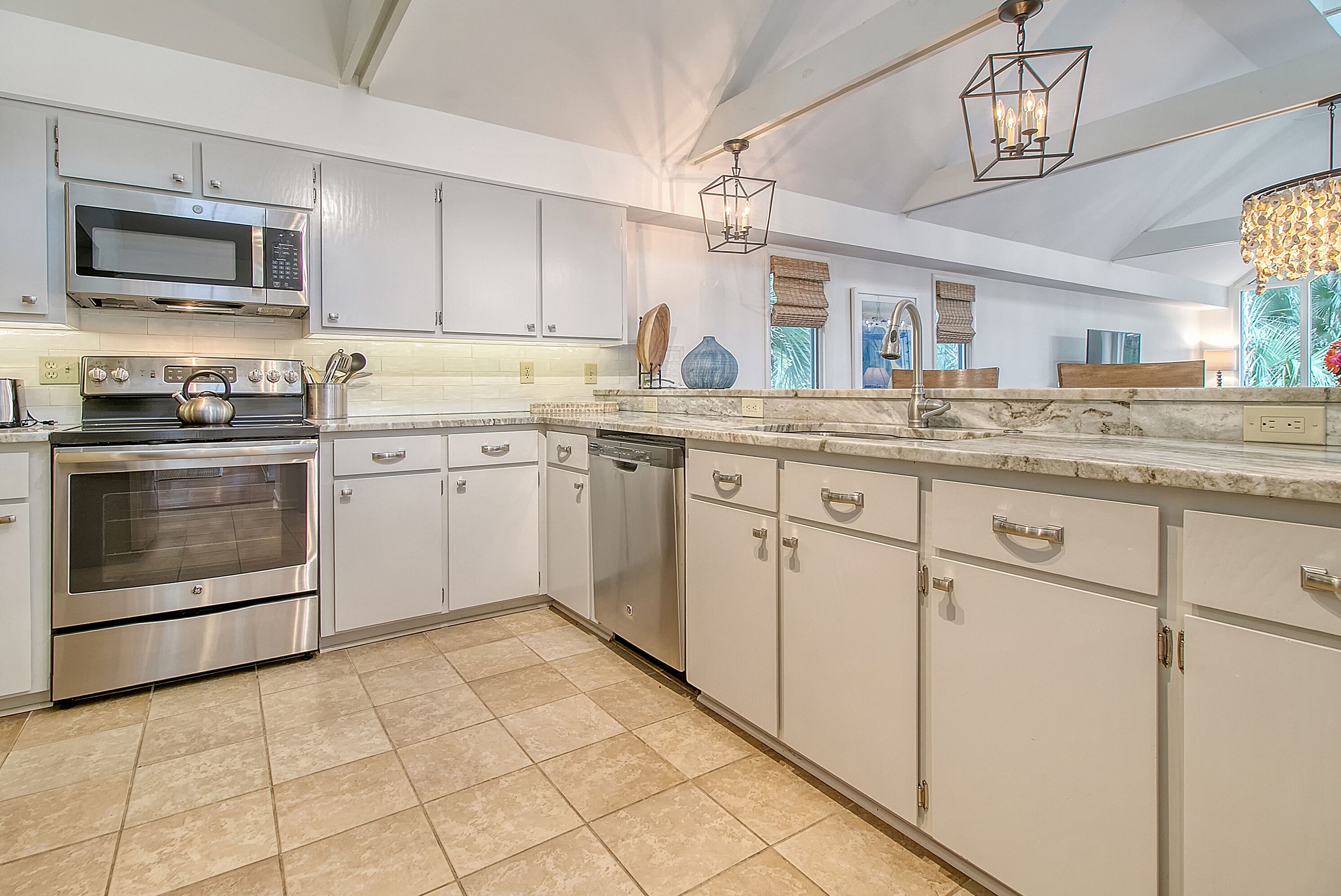 A modern kitchen with stainless steel appliances, white cabinetry, and a marble countertop.